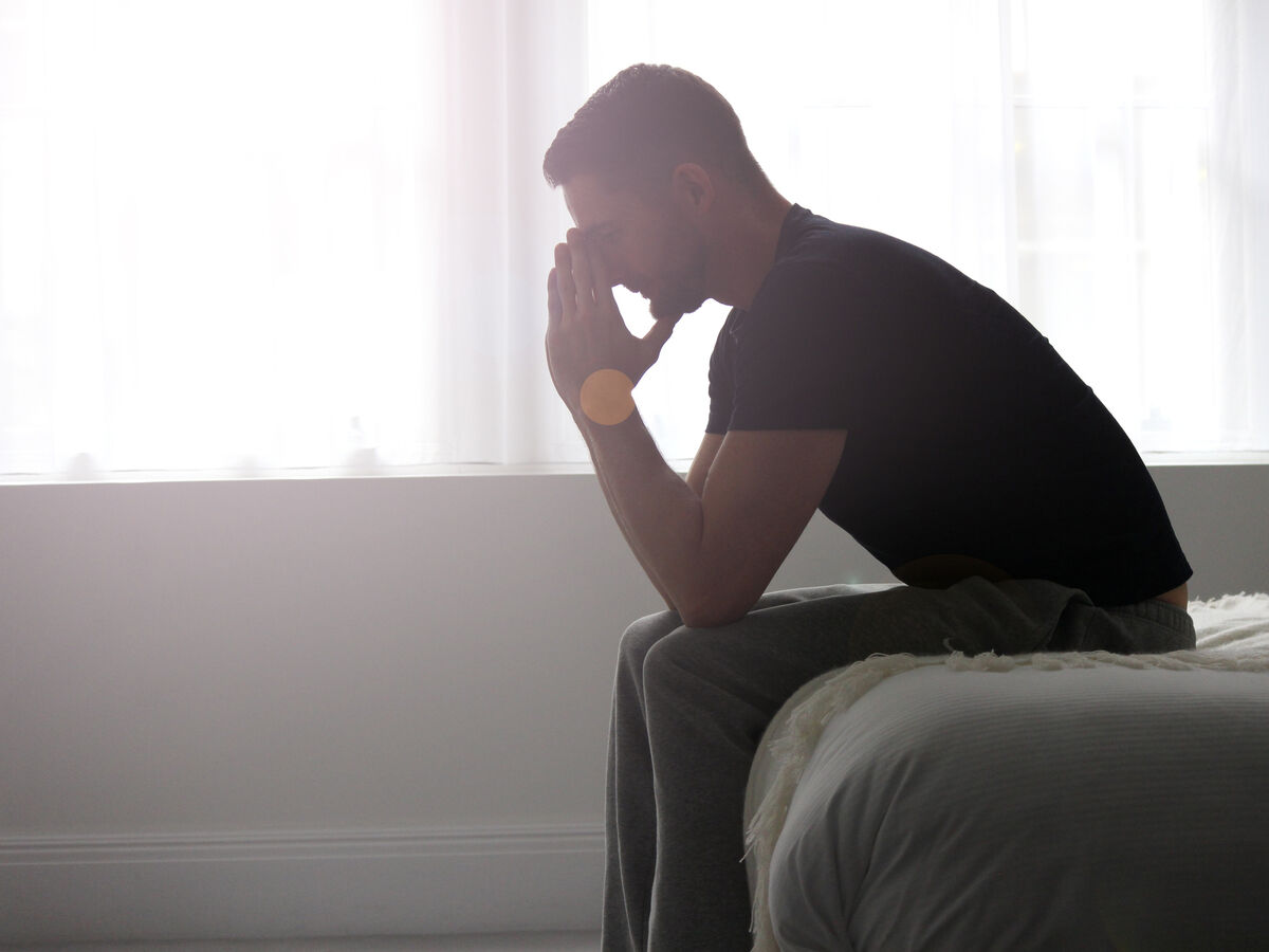 Depression A man sitting at the end of a bed, deep in solemn thought.